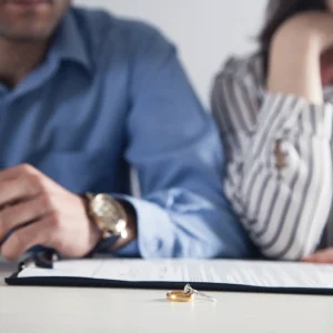 Two wedding bands lie on a white surface in front of a blurred couple, representing the complexities of divorce and separation in Minnesota